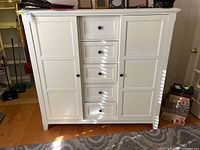 Frontal view of the white wooden armoire with five central drawers and two sliding doors closed