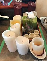 Photo showing a wicker tray holding a variety of battery operated candles: white, burgundy, green, and small white holders, plus a green decorative glass bottle with stones and lavender sprigs inside.