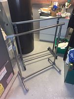 Photo of two metal and plastic adjustable coat racks in basement with various household items in background.