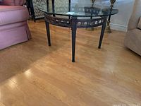 Side angle photo showing the full coffee table and its relation to surrounding furniture. Frame is black steel with decorative circular ring and tapered legs.