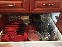Wide shot of drawer with various plastic food storage containers with red lids, glass bowls and casserole dishes.