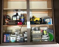 Wooden cabinet shelves with various hardware supplies including WD-40 can, caution tape, rope, and screws in plastic storage boxes.