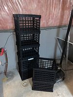 Seven black plastic crates stacked and arranged on a basement floor, showing their size, shape and material