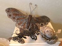 Photo showing one large steel butterfly and one small steel butterfly along with resin face sculpture on a cream surface.