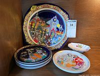 Seven plates displayed together, including one large ornate plate, five smaller decorative plates, and one white sweet meat dish with floral pattern