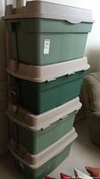 Stack of four plastic storage bins in shades of green with beige lids, stacked vertically.