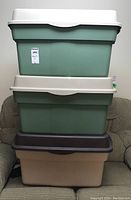 Front view of three stacked plastic storage bins: two green bins with off-white lids on top of beige bin with dark brown lid.
