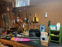 Wide view of the lot on the basement workbench and pegboard with assorted hand and power tools, household hardware, tapes, brushes, and a toilet seat.