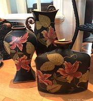 Photo showing three decorative vases with black matte finish and pink and gold floral patterns placed on wooden floor