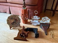Photo showing all items in the lot: 2-tier appetizer server, butterfly plate on stand, egg coddler set, ceramic orange wall sconce, and multiple plate easels of varying sizes and materials.