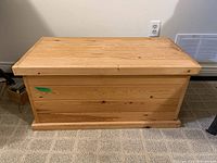 Rectangular wood chest with closed lid, natural wood finish, sitting on carpeted floor.