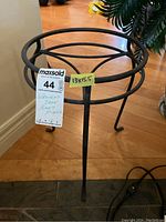 Wrought iron plant stand shown from a side angle, displaying scratches and three metal legs with circular ring supports