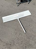 Full view of the 36-inch paint edger, white metal surface and handle shown on pavement.