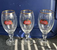 Three large Stella Artois branded pint glasses shown standing upright, clearly displaying the red and white logo and gold rims.