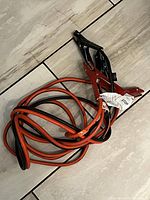 Coiled booster cables with red and black insulated wires and metal clamp connectors on tiled floor.