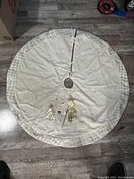 Full view of round white Christmas tree skirt showing embroidered Santa, trees, and snowflakes.