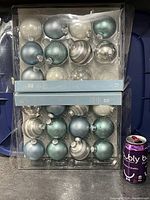 Photo showing two unopened packages holding 12 glass Christmas ball ornaments each in blue, white, silver, and glitter finishes, next to a soda can for scale.