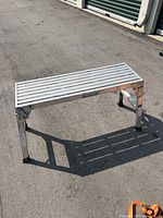 Folded scaffold step platform showing aluminum slatted surface and collapsible legs locked in position.