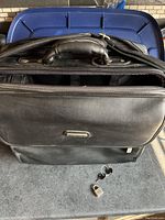 Soft black vinyl business briefcase with multiple zippered compartments, handle and shoulder strap, shown closed with original padlock and two keys placed in front.