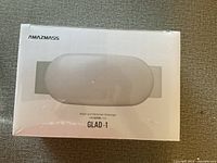 Front of the box showing the product and branding Amazmass GLAD-1 waist and abdomen massager in white and grey colors.