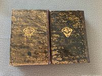 Photo of two leather-bound Hebrew books with worn brown covers and gold emblems, showing front covers.