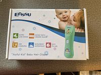 Box front showing branding, product name, key features (super low-noise, dense-teeth ceramic blade, USB charging, waterproof, easy to use), and a photo of the clipper with a baby and mother.