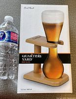Front view of the original box showing the Quarter Yard beer glass on its wooden stand next to a water bottle for scale.