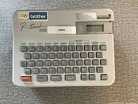 Top view of Brother P-touch 2000 label maker showing keyboard, LCD screen, and printed label.