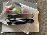 Photo showing two plush mice cat toys with multi-colored feather tails sealed in plastic bags along with a silver metal laser pointer pen inside a foam-lined metal case.