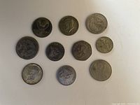 Top-down photo of 10 coins on white background showing various designs including portraits and emblems.