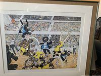 Framed lithograph showing a basketball game scene with players in yellow and blue uniforms on a court with audience.