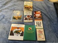 Eight cooking and health-related books laid out on a blue fabric surface including vegetarian, diabetic menus, tea tree oil, and calorie counting guides.