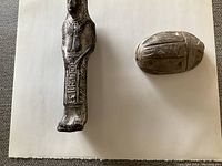 Side view of standing figurine and oval scarab figurine showing detailed carvings
