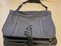 Front view of black Samsonite garment bag with zipper and adjustable shoulder strap.