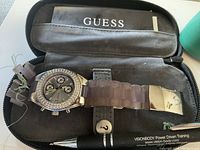 GUESS women's wristwatch displayed inside the soft GUESS branded zippered case along with instruction manual and a pen for scale reference.
