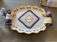 Oval ceramic challah plate with colorful figures on each side and decorative painting.