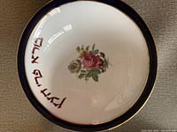 Top view of Judaica plate showing floral design and Hebrew lettering with black and gold rim