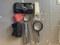 Overall collection of magnifying glasses and optical accessories laid on floor showing all included items and their general condition.
