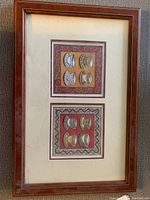 Framed artwork featuring stylized cup prints in two sections within a wood frame and glass cover.