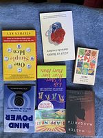 Top view of seven books arranged on a fabric surface, showing front covers of each book including 'One Simple I', 'Mind Power', and others.