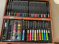 Open view of the art set showing colored pencils, watercolor paints, oil pastel tubes, markers, sharpener, and eraser inside.