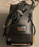 Top view of black Sony cassette recorder showing perforated speaker grill, strap, and coiled power cable with two-prong plug.