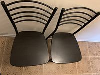 Top view of two black chairs with wooden seats and curved metal backs with horizontal bars.