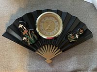 Full view of fan-shaped wall clock showing black sections with floral patterns and central clock face.