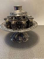 Front angle view of the full wine fountain with 8 cups on a detailed pedestal base showing floral and grapevine decorations.