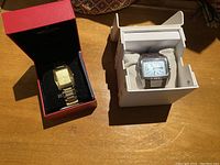 Both watches shown in their respective boxes on a wooden surface.