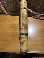 Full view of wooden or bamboo African stringed instrument with decorative carvings and hair/fur bands, shown on wooden table with fabric background