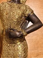 Close-up of the dancer's torso showing intricate gilt floral and geometric patterns on the costume and the bronze arm.