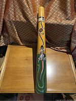 Full view of hand painted Australian Aboriginal didgeridoo with intricate dot painting and animal design motifs, positioned vertically on wooden surface.