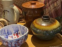 View of the pottery items including vases, a bowl, jar with lid, and decorative tile holders on a wooden tray with patterned fabric background.
